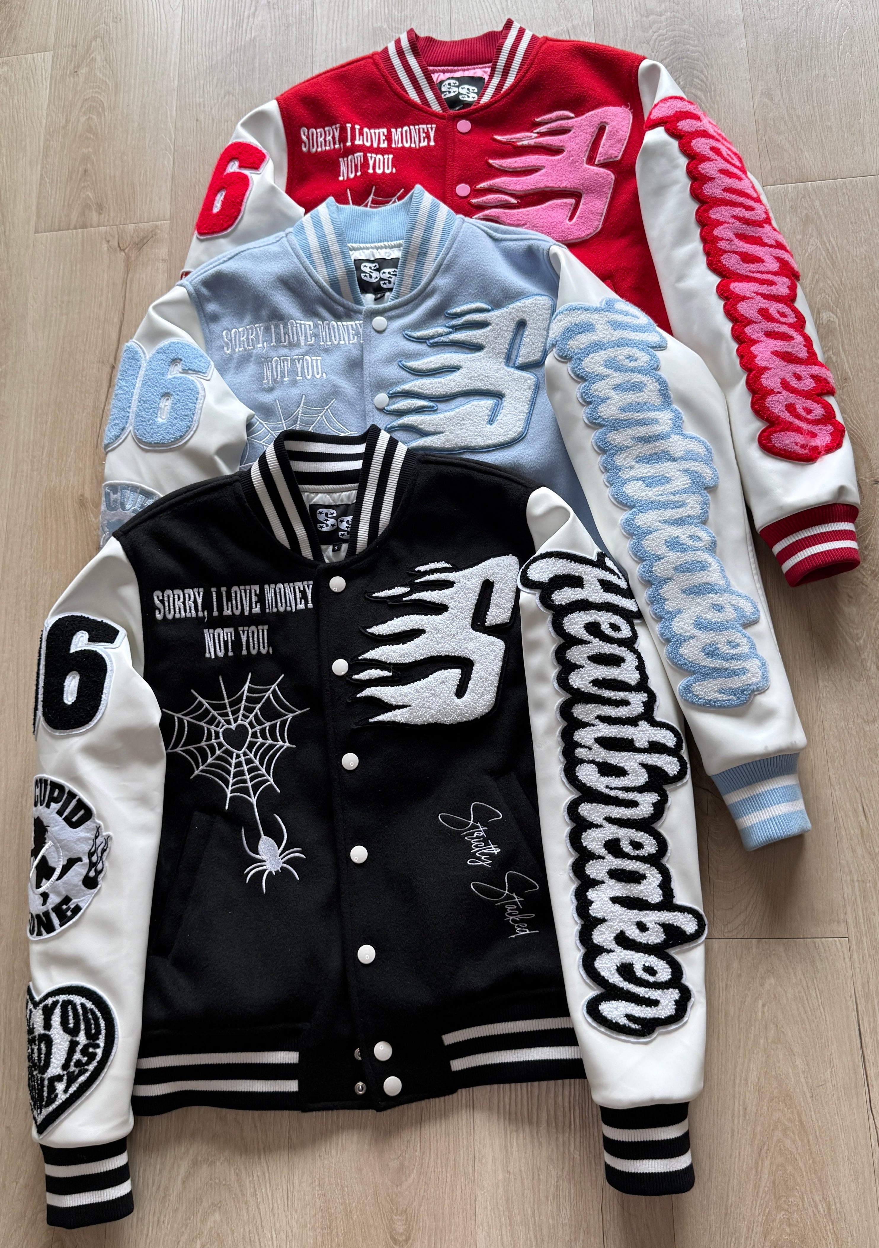 Three varsity jackets in different colors on a wooden floor.